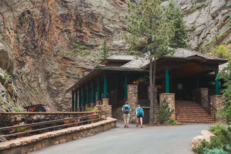 A Couple Of People Walking Into A Building With A Mountain In The Background