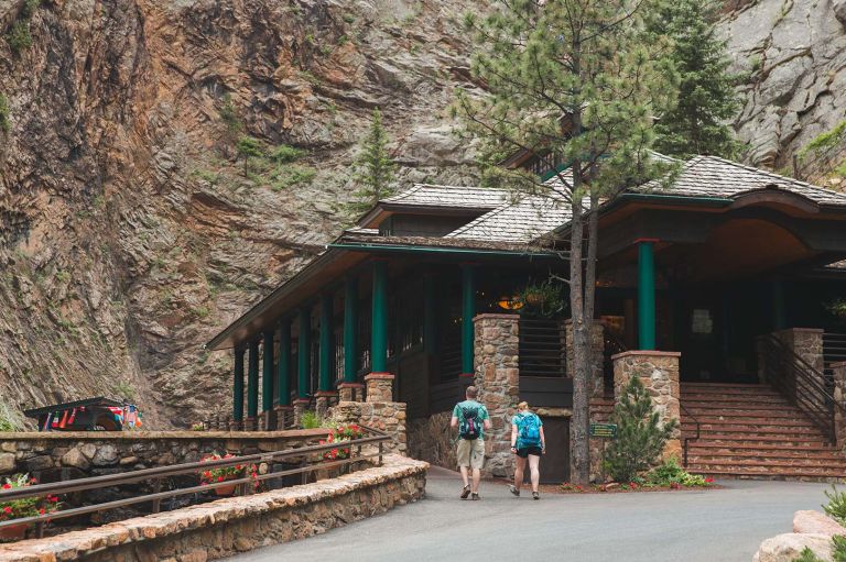 A Couple Of People Walking Into A Building With A Mountain In The Background